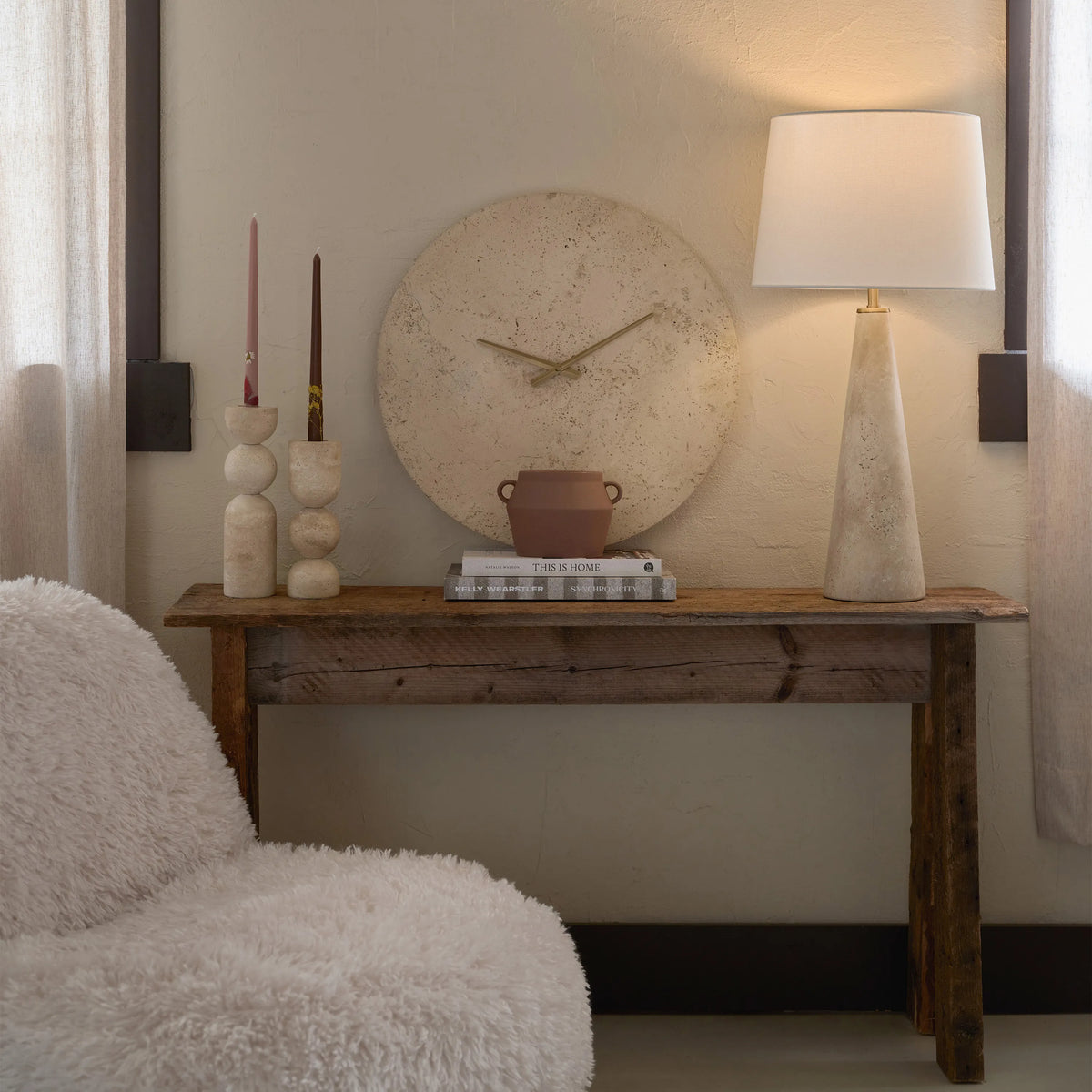 Solea Travertine Wall Clock styled on rustic console table with lamp and candles in cozy neutral room