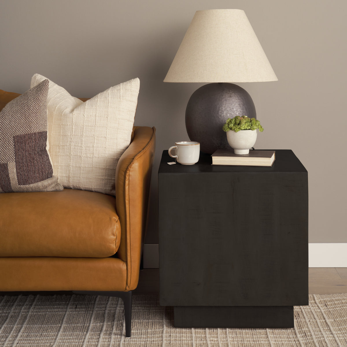 Dark brown side table with lamp, mug, and plant next to a brown leather sofa.