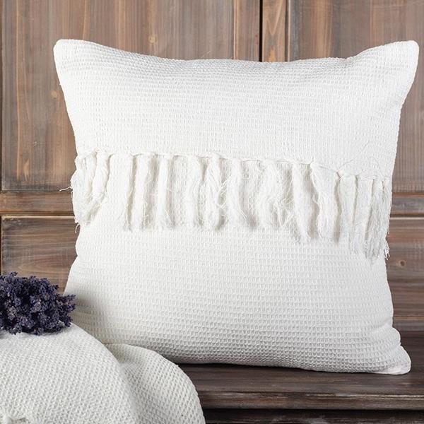 White textured pillow with tassels on a wooden surface