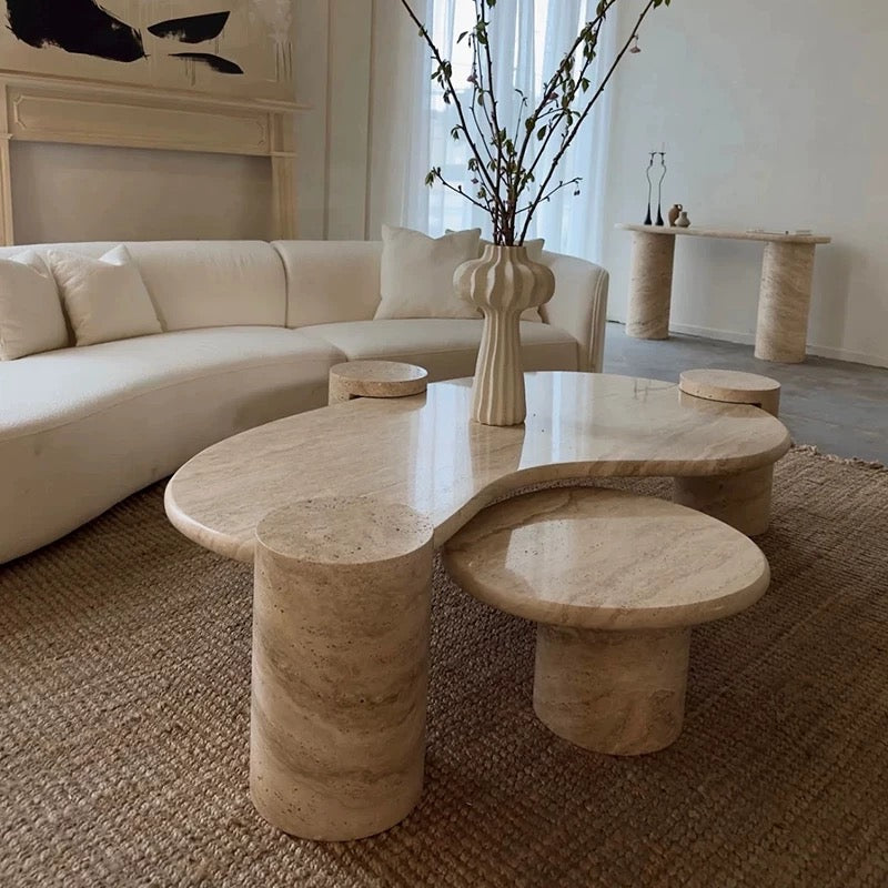 Angled view of the Ardea travertine stone coffee table set in a modern minimalist living room with abstract art.