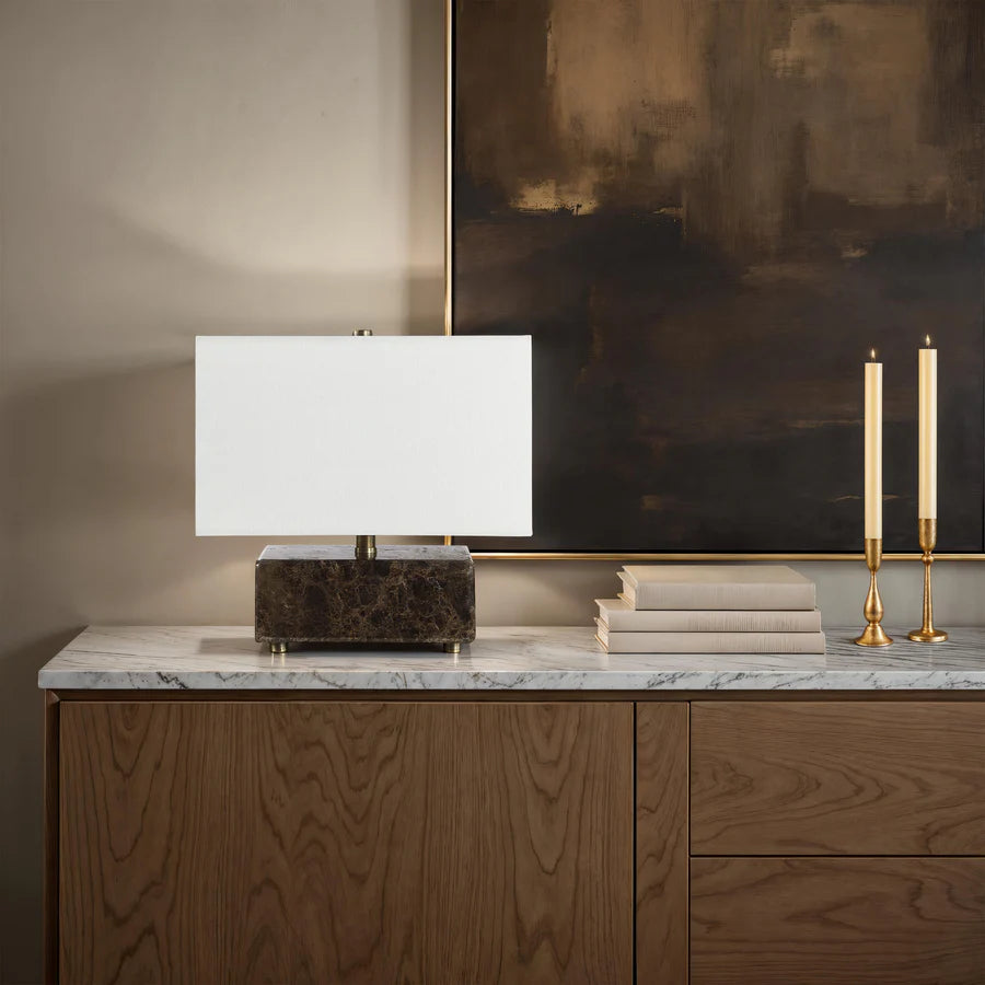 Modern lamp on a marble surface with candles and books against an abstract painting.