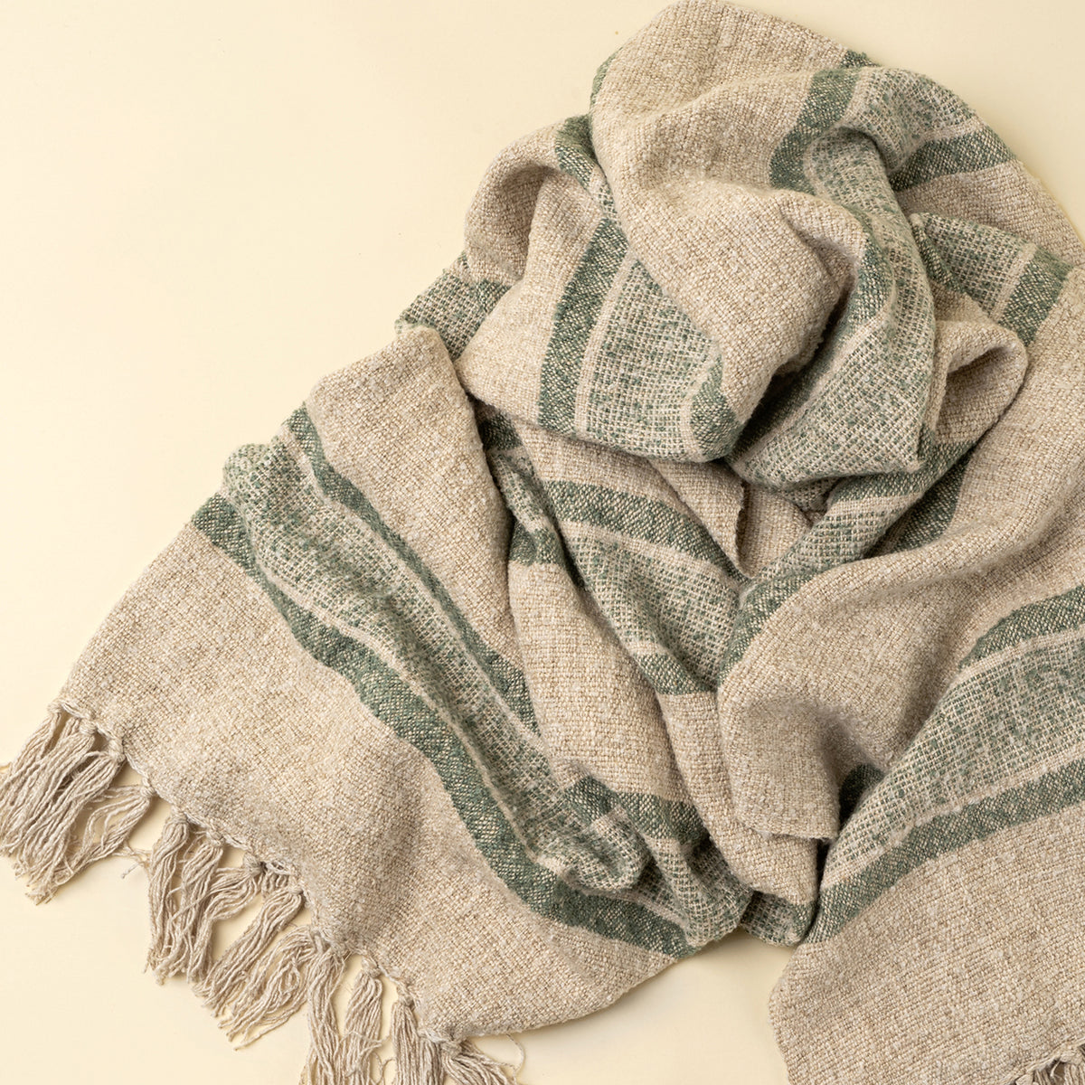 Textured scarf with green stripes and tassels on a beige background