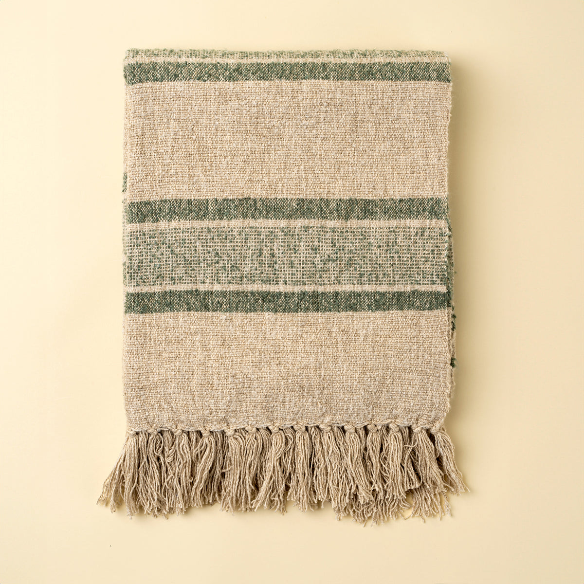 Textured blanket with green stripes and fringes on a beige background