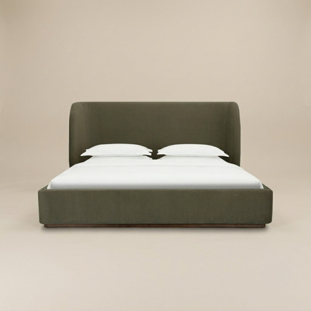 Aveline bed with a tall curved headboard and matching footboard in a muted olive green color velvet fabric, set against a plain beige studio background.