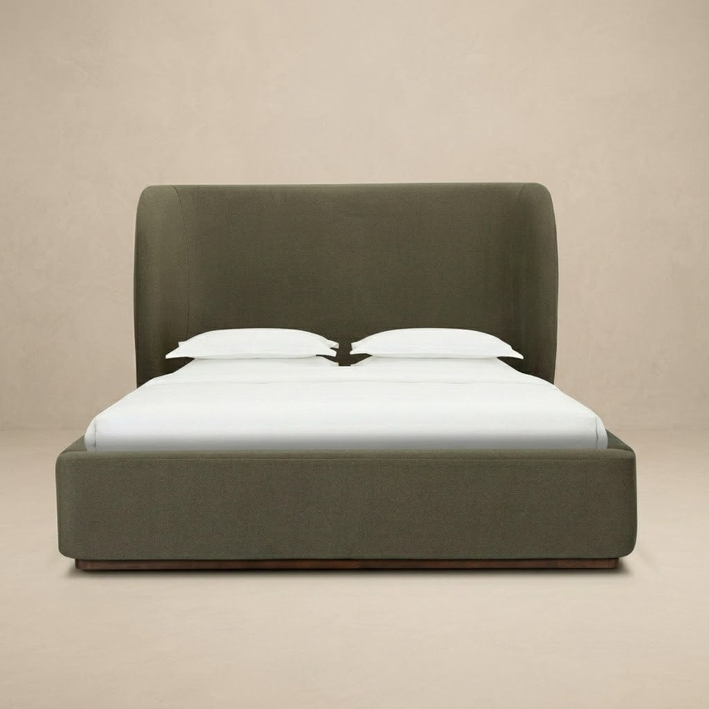 Aveline bed with a tall curved headboard and matching footboard in a muted olive green color velvet fabric, set against a plain beige studio background.