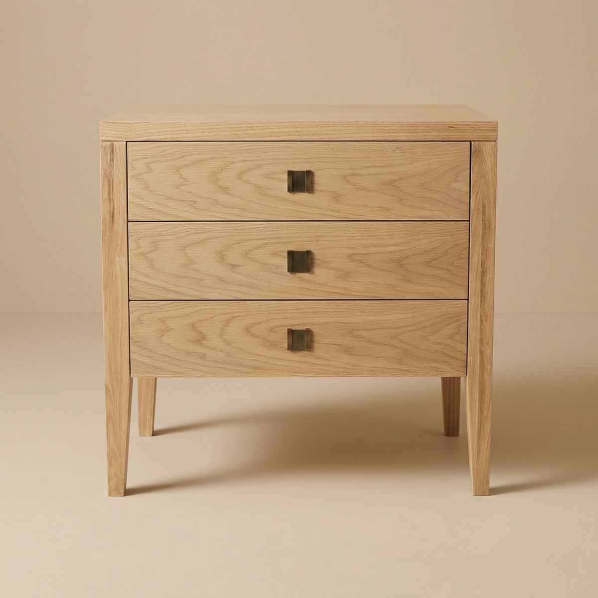 A straight-on studio shot of the Beaumont 3-Drawer Nightstand in Natural Oak, featuring three even drawers with centered brass hardware.