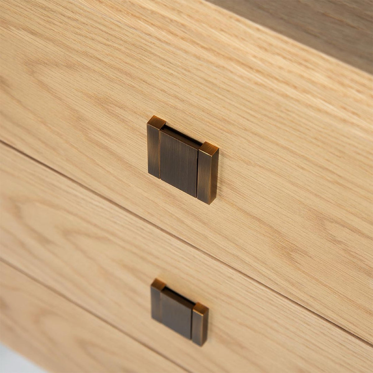Macro detail shot of the Beaumont Nightstand's antique brass drawer pulls against the natural oak wood grain texture.