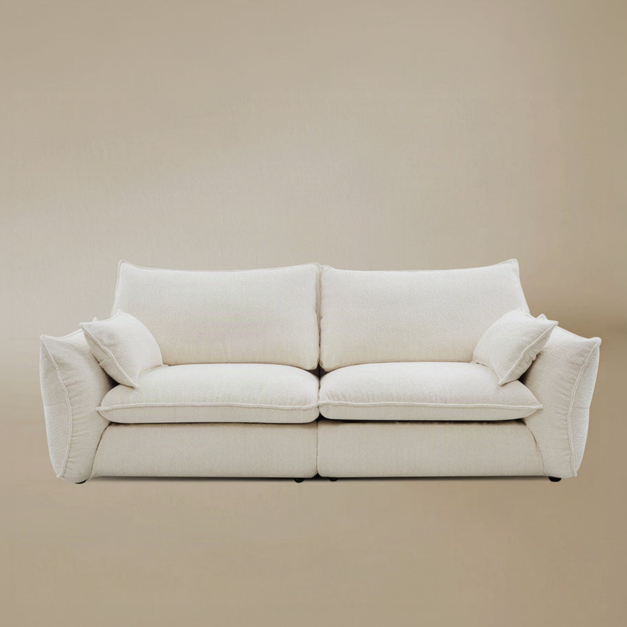 Bella Boucle Sofa upholstered in cream boucle fabric, featuring oversized square back cushions, with matching throw pillows on the side, and flared armrests, set against a solid beige studio background.