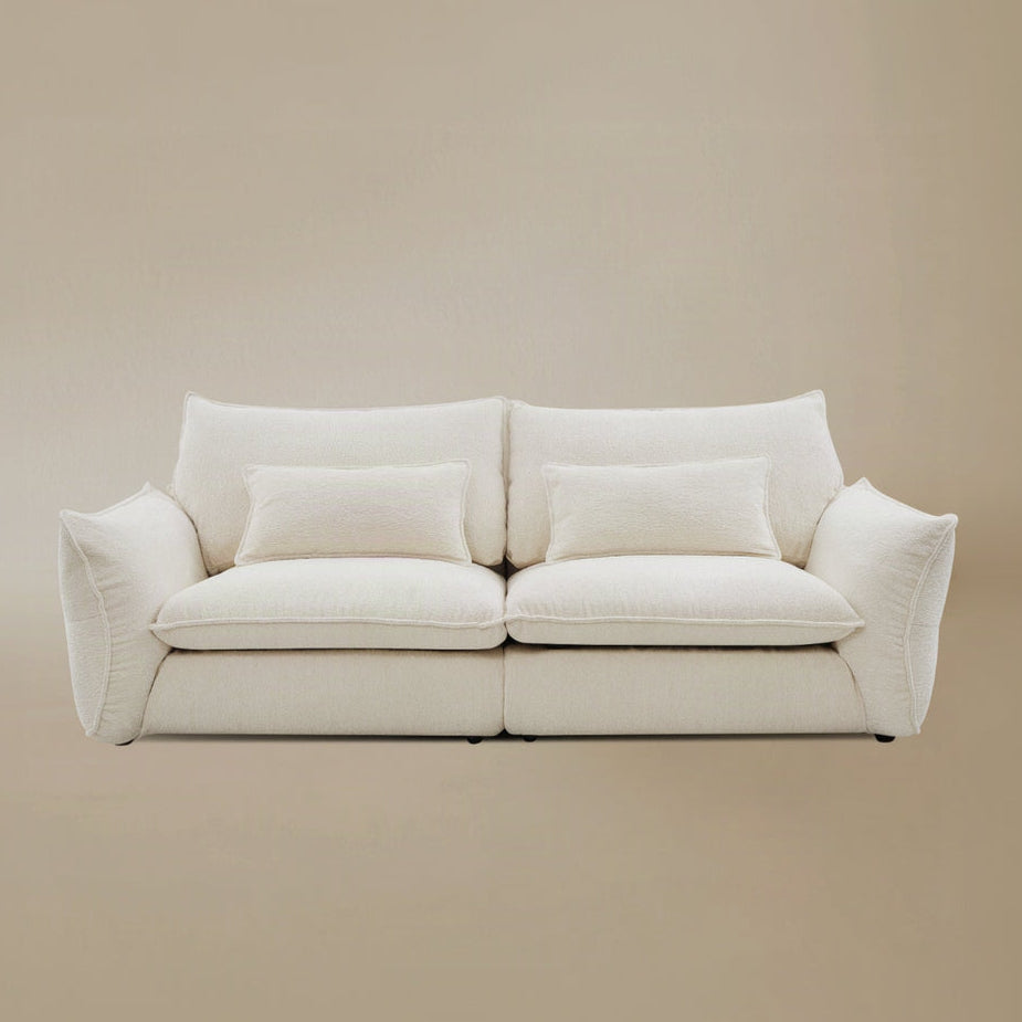 Bella Boucle Sofa upholstered in cream boucle fabric, featuring oversized square back cushions, matching throw pillows, and flared armrests, set against a solid beige studio background.