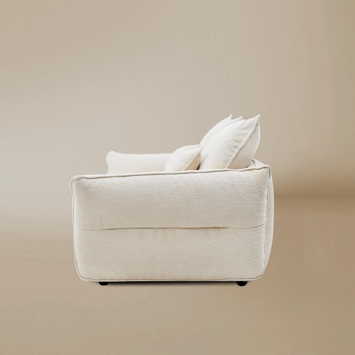 Bella Boucle Sofa in cream boucle fabric, shown from a rear angle with matching throw pillows, set against a warm beige studio background.