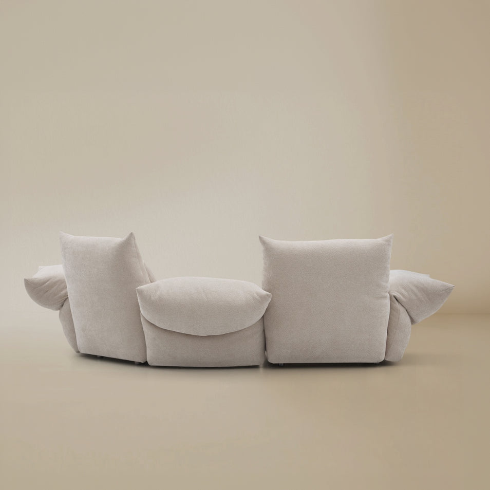 Back profile of the modular Blooming Embrace Modular Sofa in pearl chenille fabric with plush cushions and curved silhouette on beige studio background