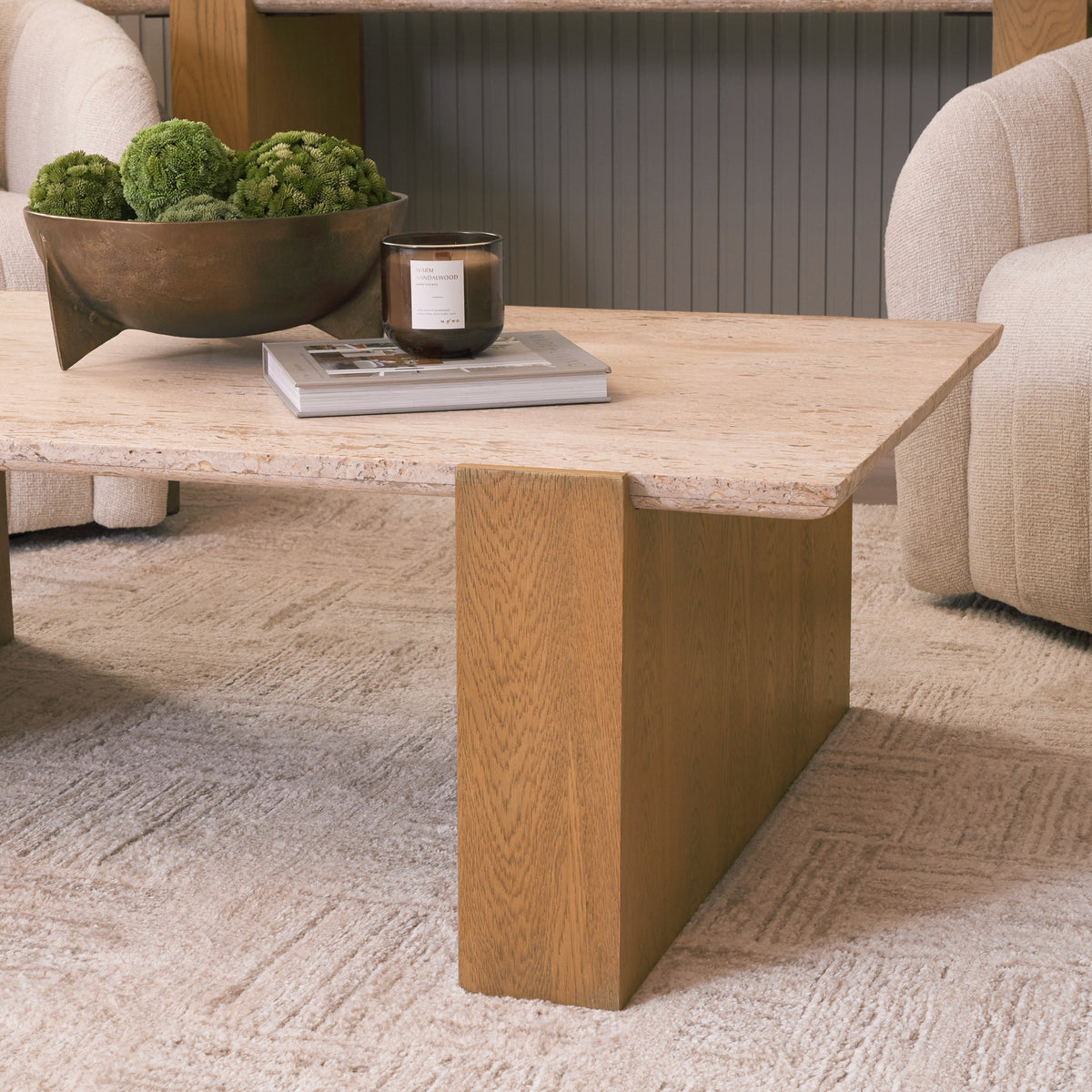 Lifestyle detail of the Cavelle Travertine & Oak Coffee Table showing the stone top and oak leg styled between upholstered lounge chairs.