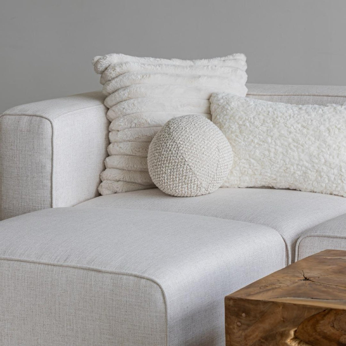The Cloudline textured cushion trio styled on a cream bouclé sectional sofa next to a live-edge wood coffee table.
