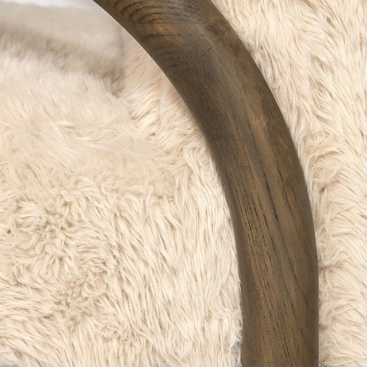 Close-up detail of the Coco chair's arched armrest showcasing the smooth dark walnut wood grain against the shaggy sand fur.