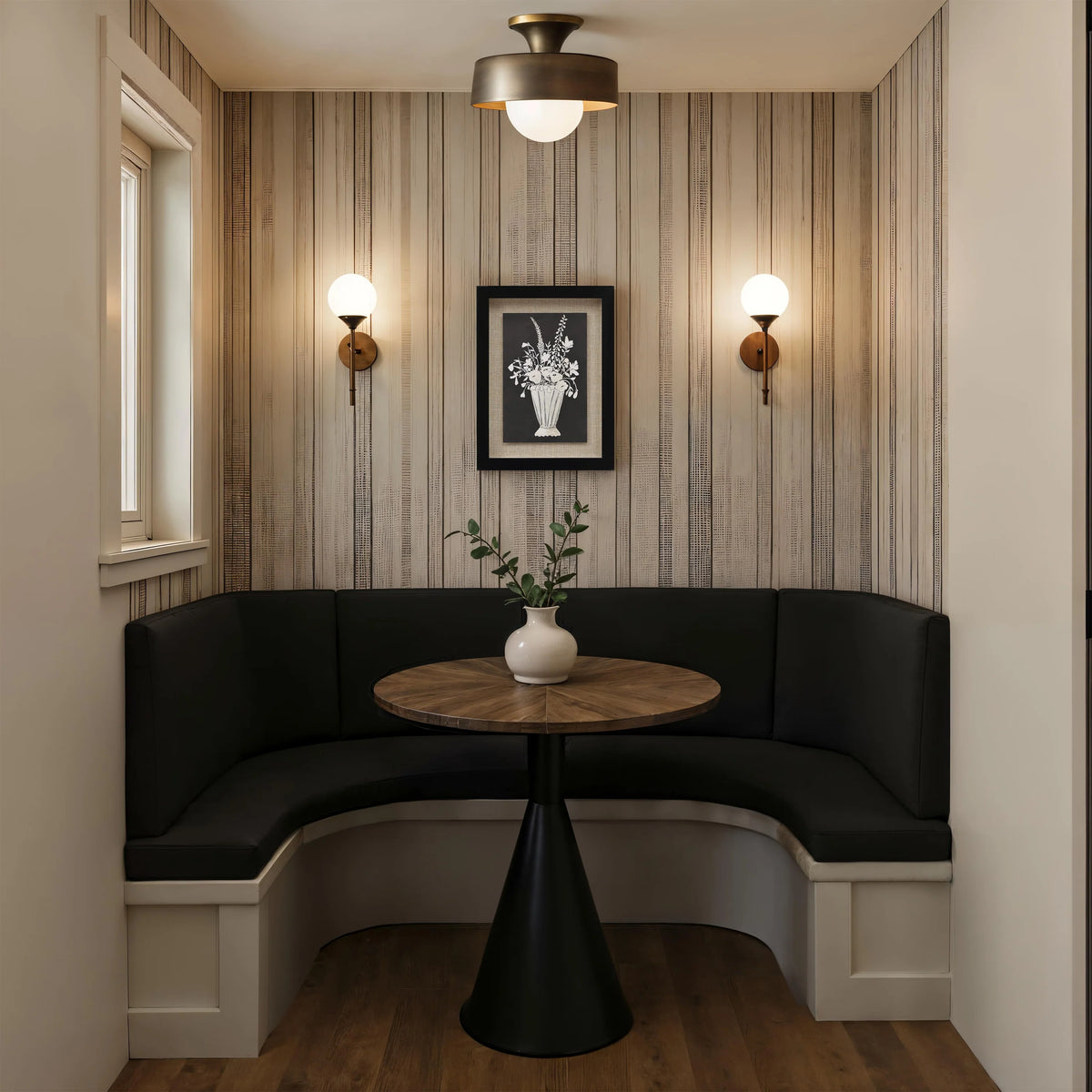The Daphne botanical wall art hanging above a dark corner banquette seating area with a round wooden table and wall sconces.