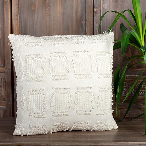 Textured white pillow on a wooden surface with a wooden wall and plant in the background