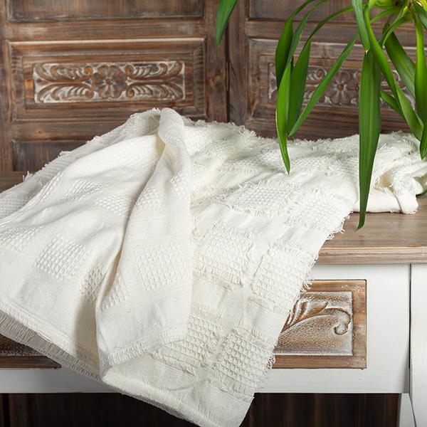 White textured blanket draped over a wooden bench with decorative carvings.