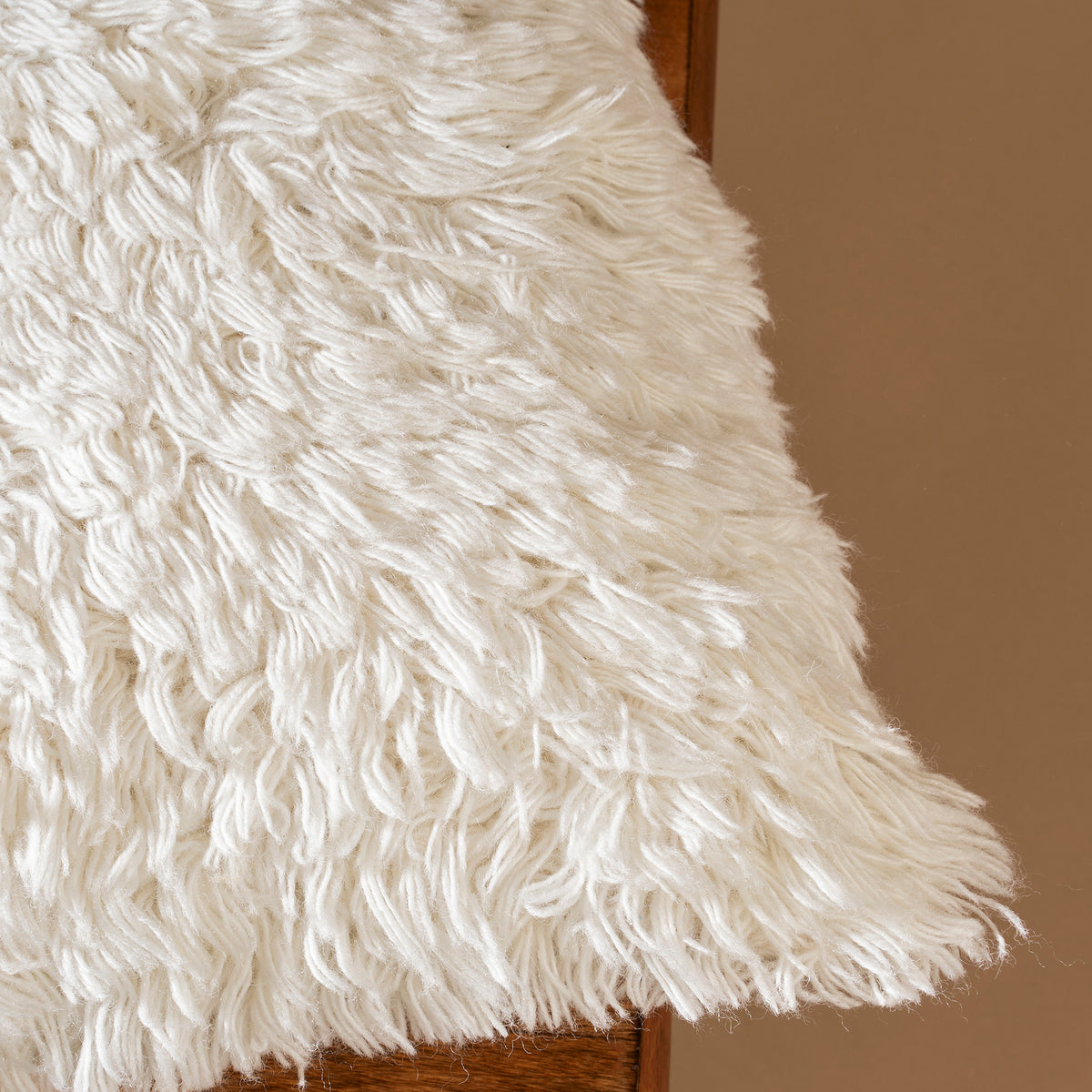 Close-up of a fluffy white rug on a wooden surface with a brown background