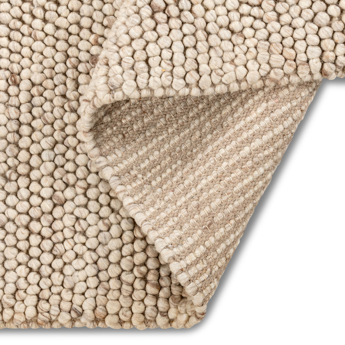 Folded corner of the beige Felix handmade textured rug, revealing its chunky pebble-like surface and durable backing