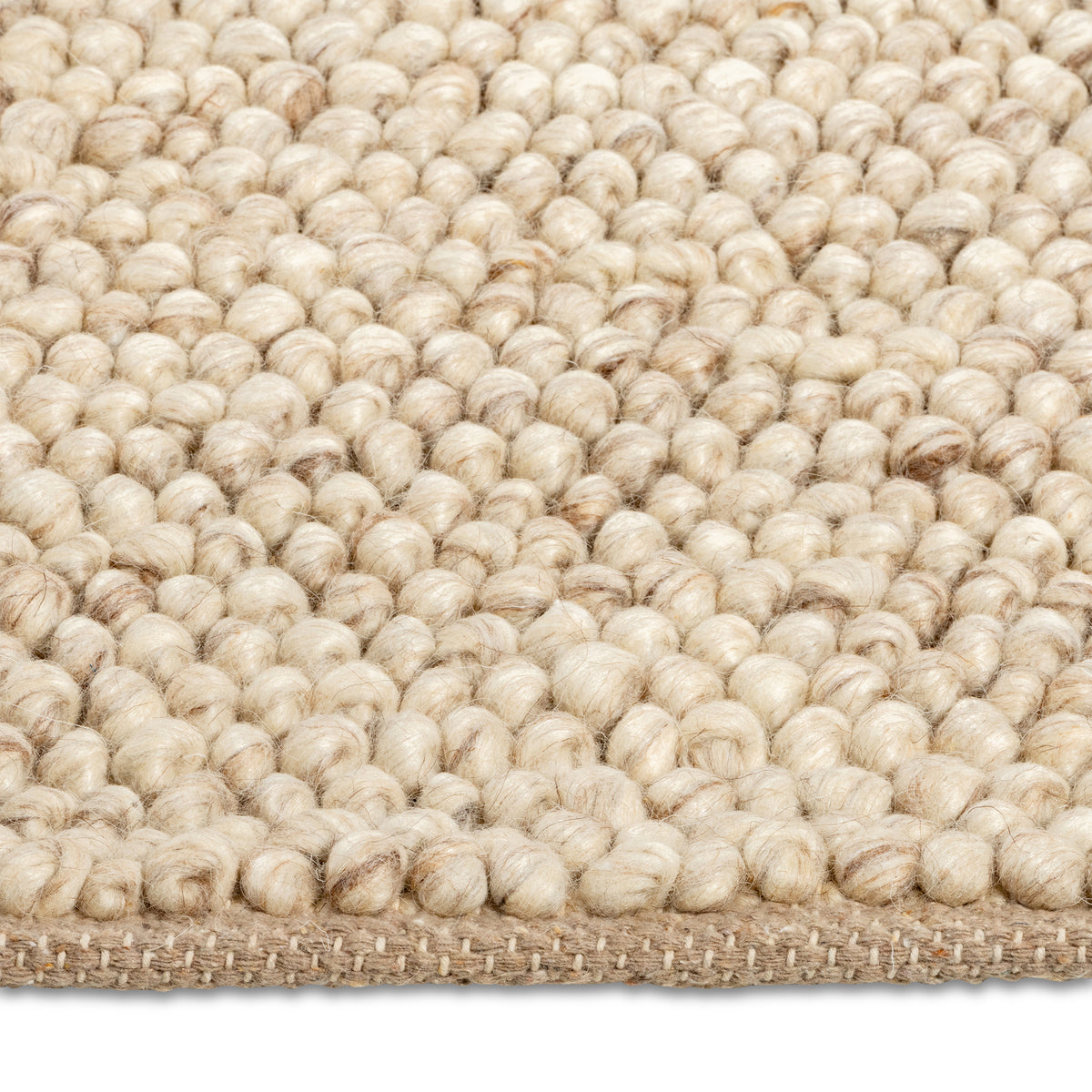 Macro close-up of the soft, pebble-like knotted texture of the beige Felix handmade rug.