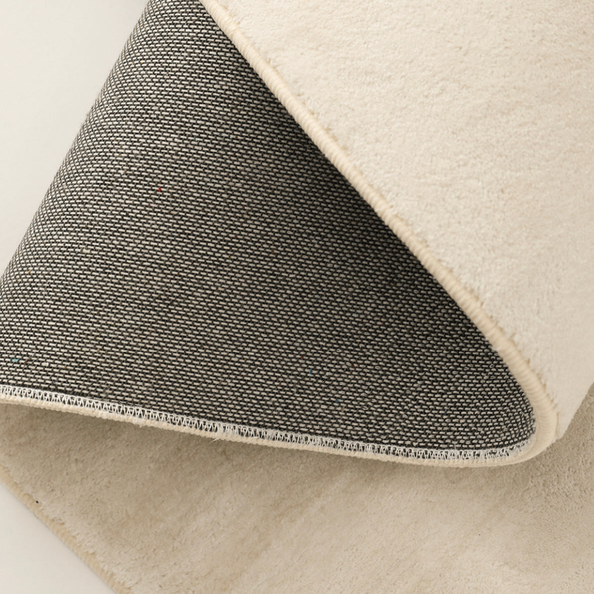 Folded corner of the Isabella Rug showing the cream pile, bound edge and dark woven backing