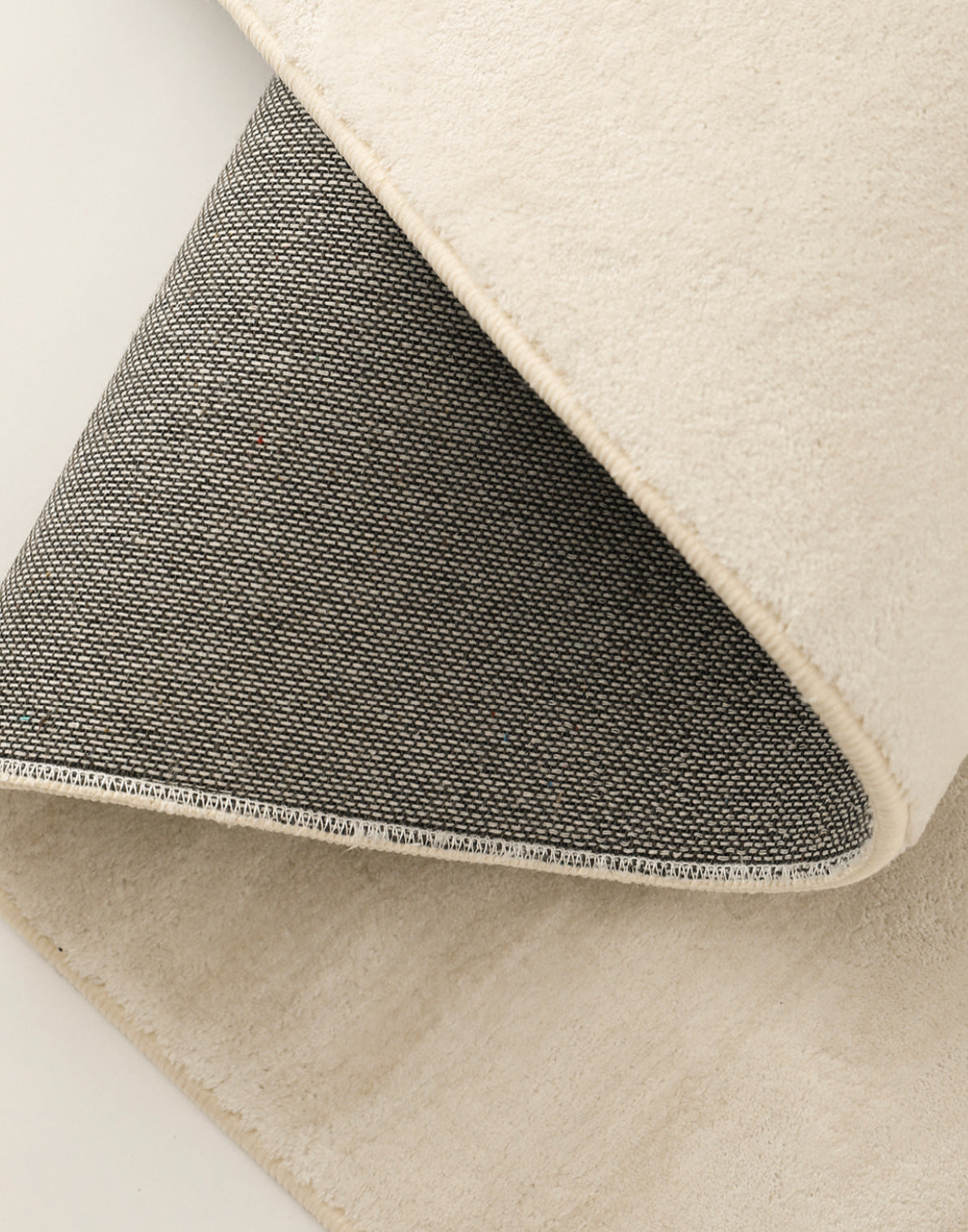 Folded corner of the Isabella Rug showing the cream pile, bound edge and dark woven backing