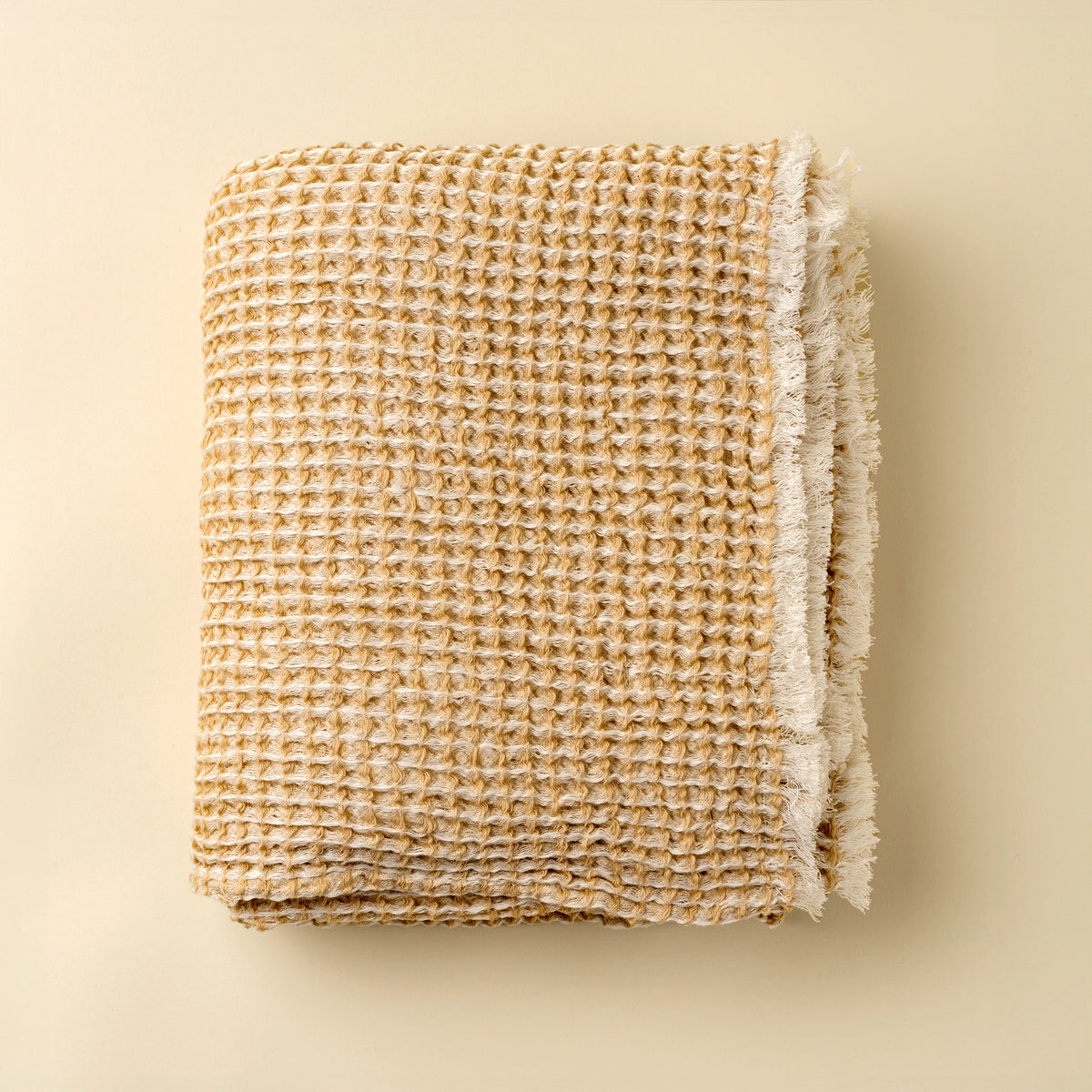 Folded woven blanket with frayed edges on a beige background
