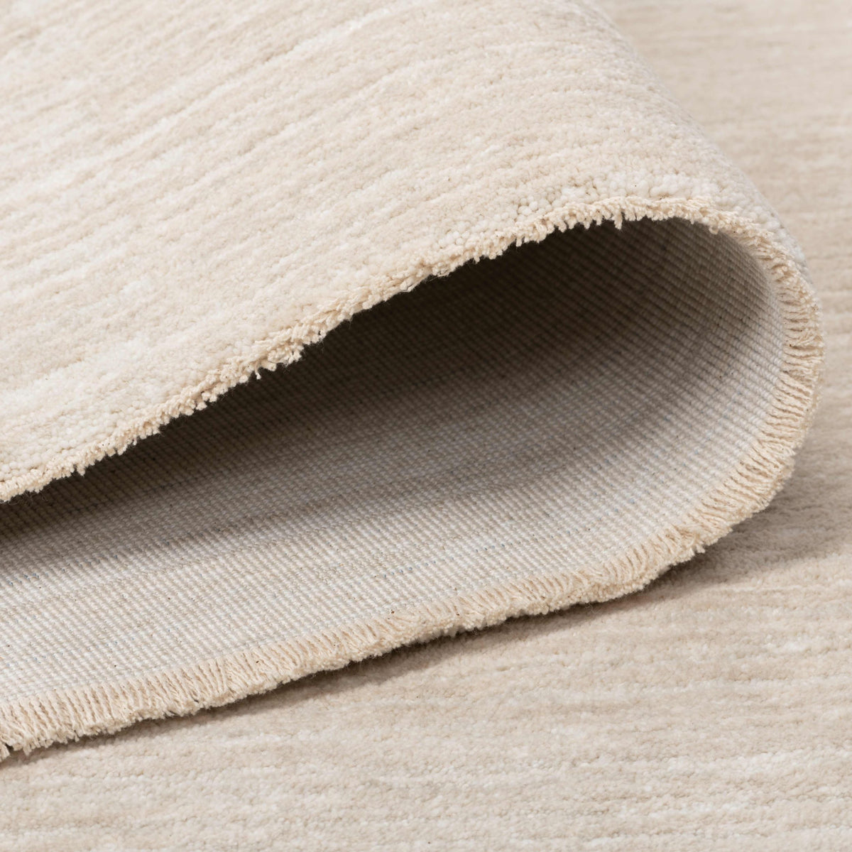 Folded edge of the Jeanne Rug showing its soft low pile and woven backing