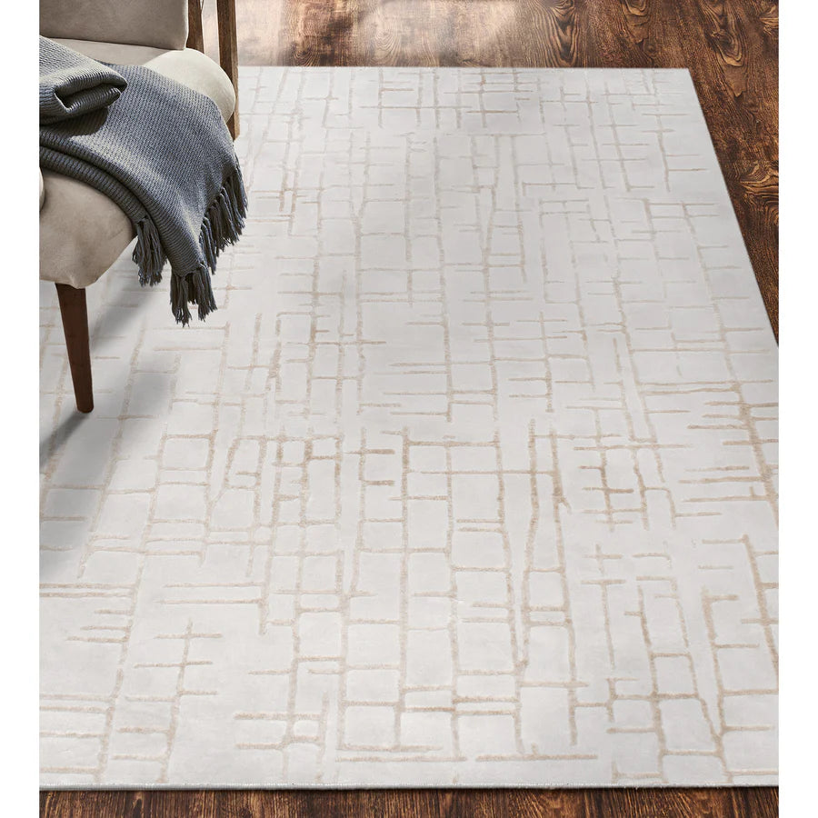 White patterned rug on a wooden floor with a chair and blanket in the corner.