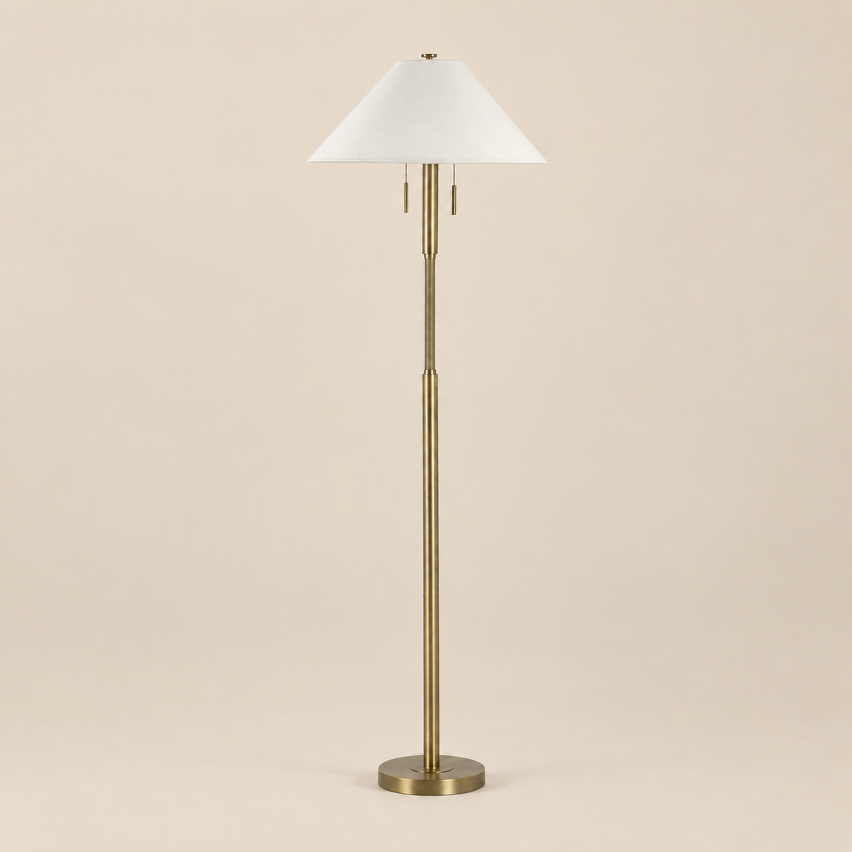 Lucienne Antique Brass Floor Lamp featuring a slender brushed brass iron stem, twin pull chains, and off-white linen shade on a seamless beige studio background.