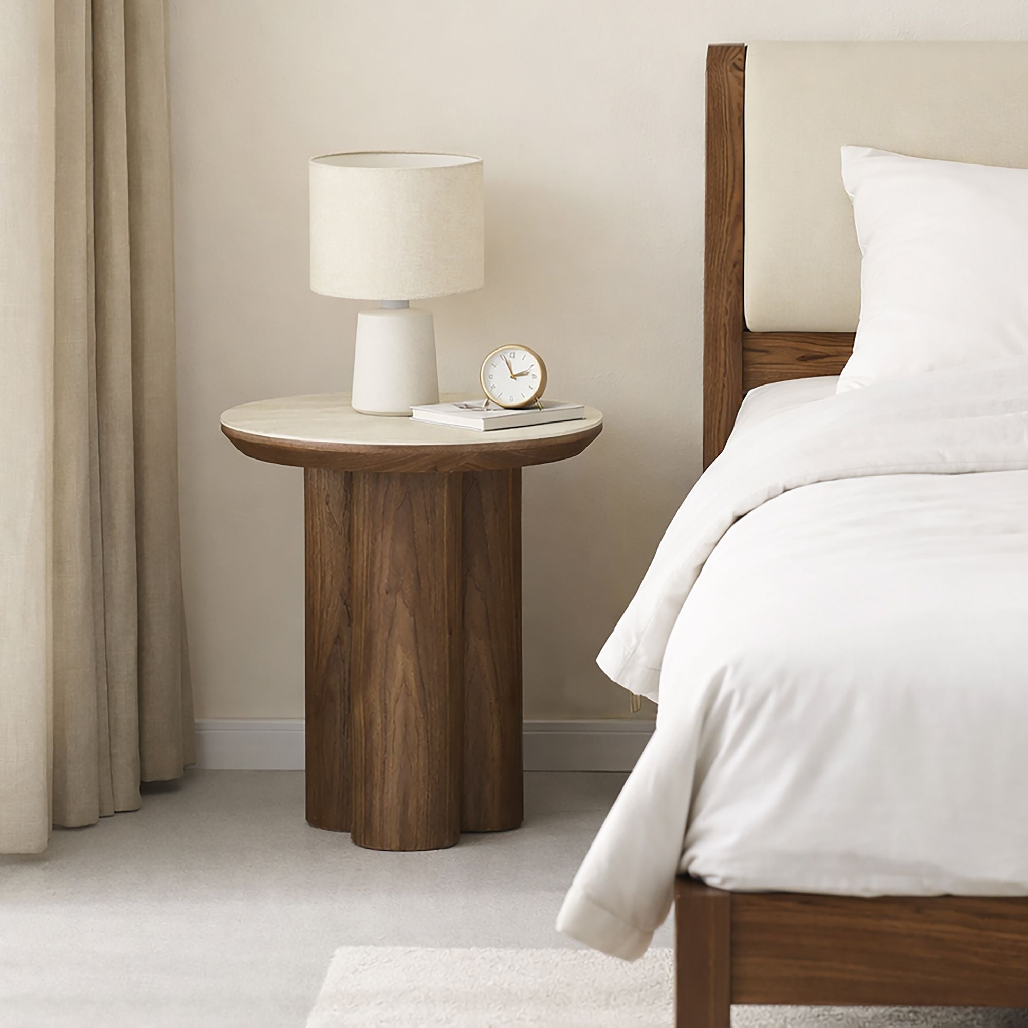 Wooden side table with lamp and clock next to a bed in a bedroom setting