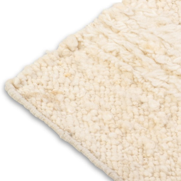 Close-up corner detail of the Maeve rug showing the neat edge binding and the contrast between the flatweave base and raised nubby wool pile