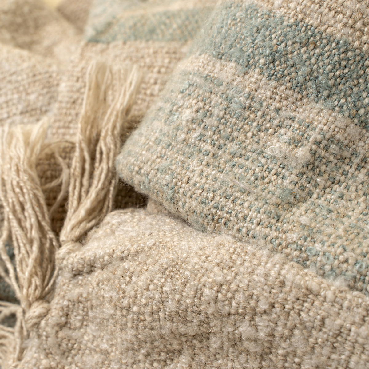 Close-up of textured fabric with natural tones and a tassel.