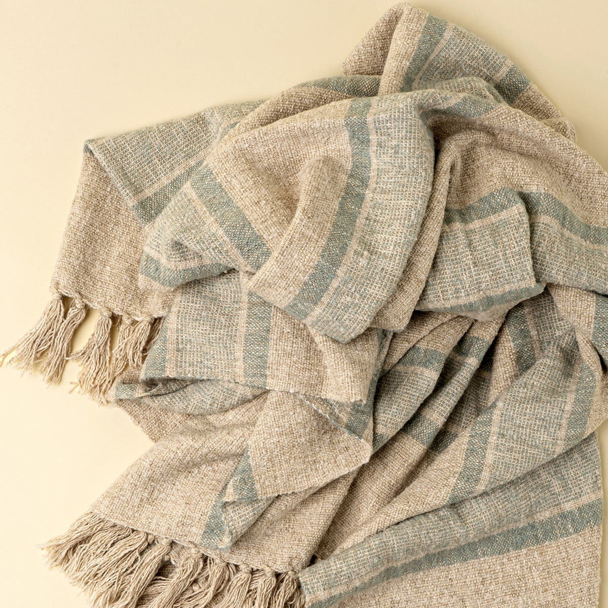 Textured blanket with blue and beige stripes and tassels on a beige background