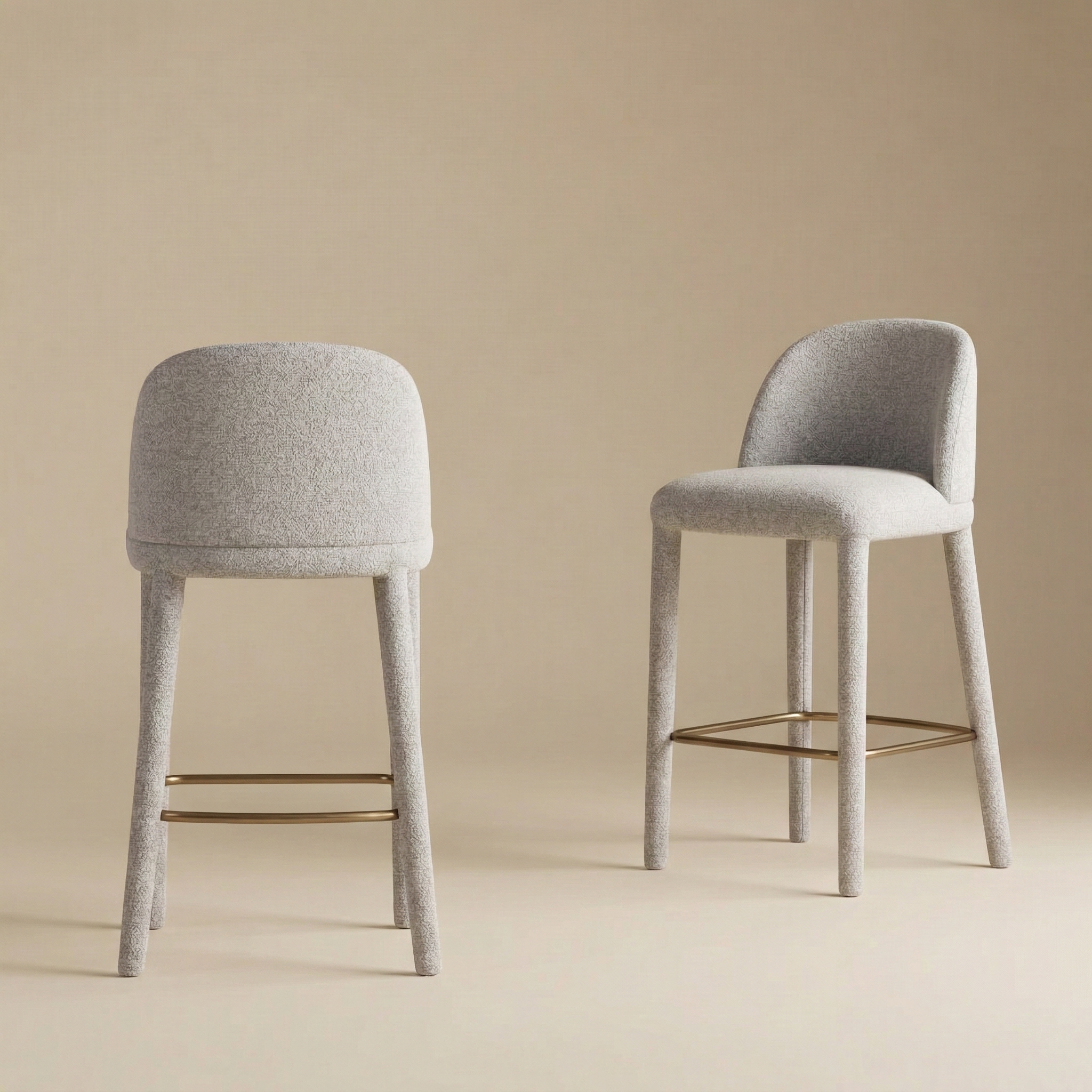 A pair of Myla upholstered counter stools showcasing the curved backrest and seamless textured beige fabric design.