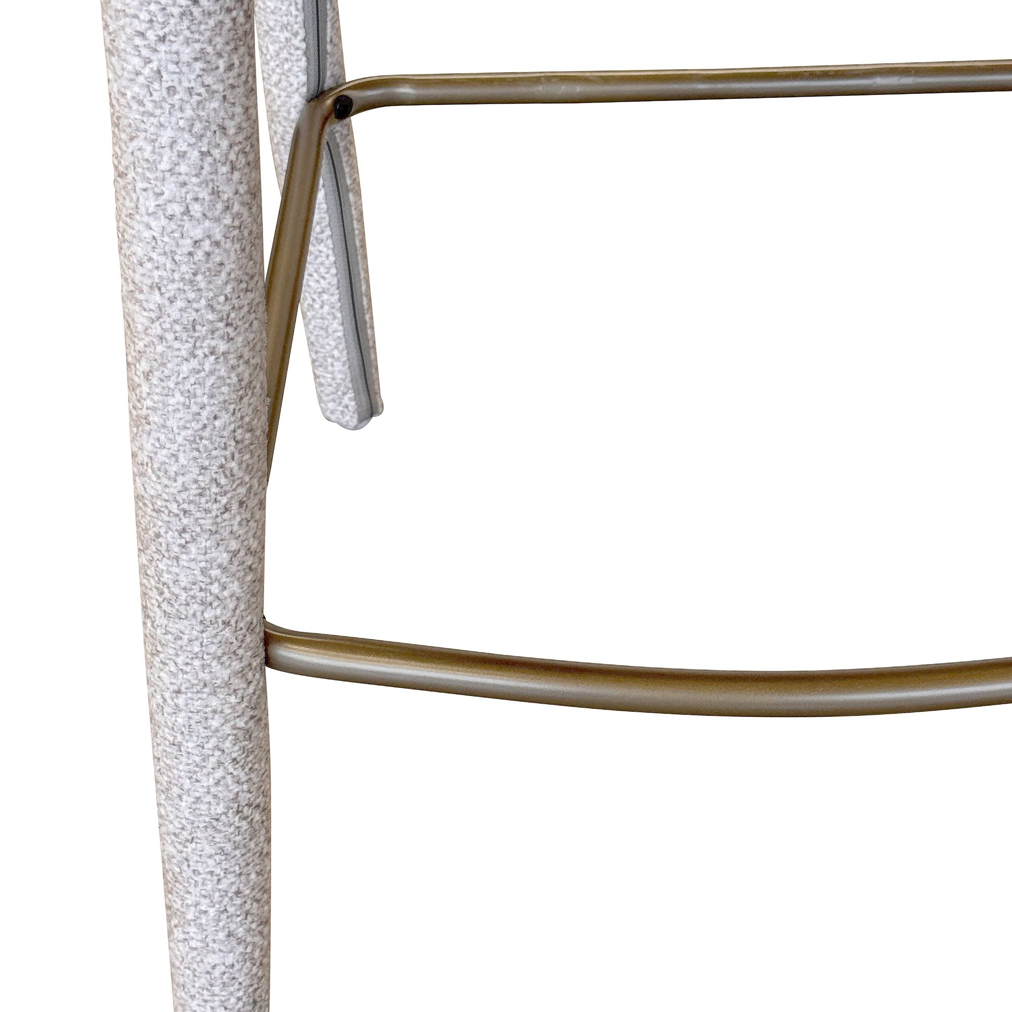 Close-up detail of the Myla counter stool highlighting the nubby, textured beige fabric on the leg and the curved brass metal footrest.