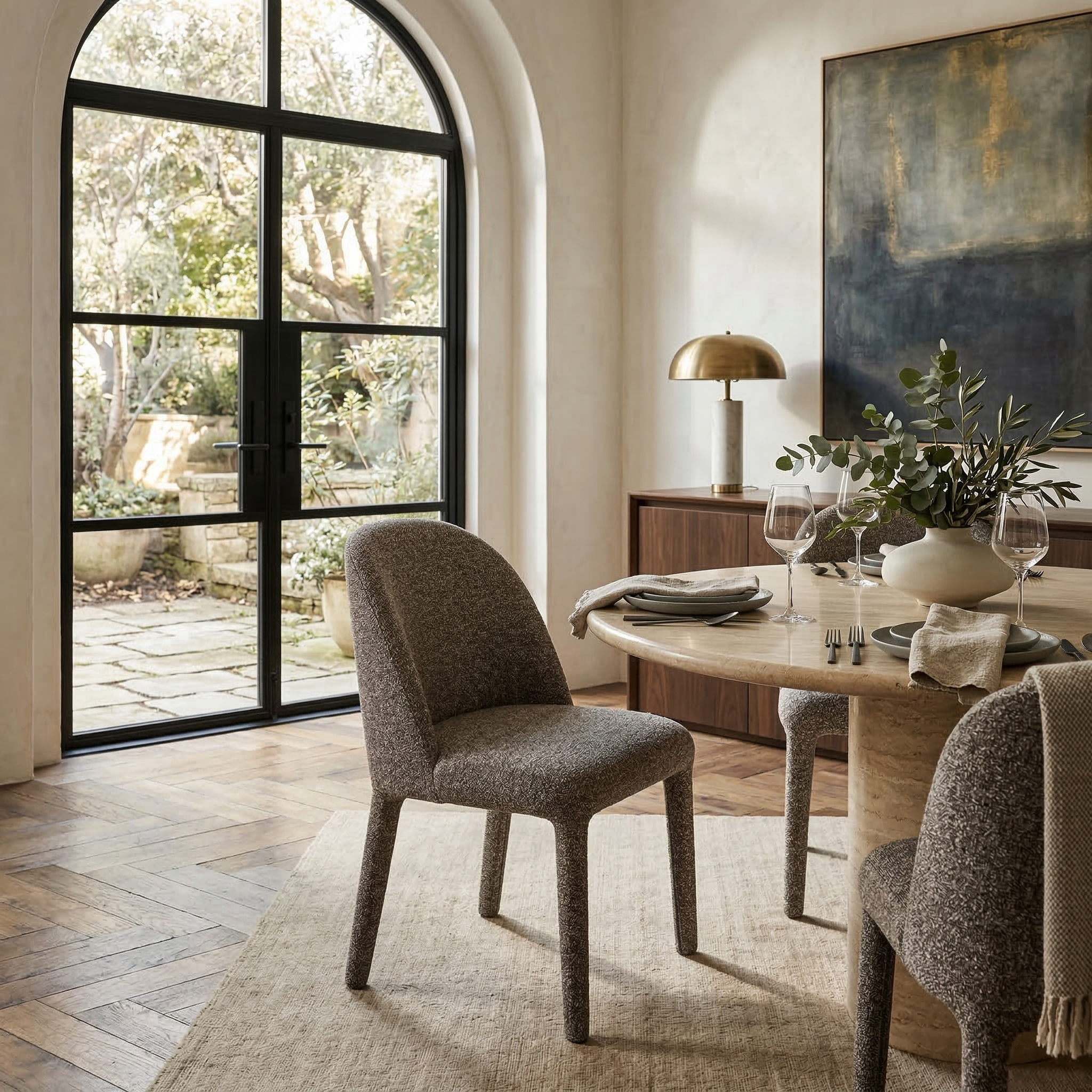 Four textured dark brown Myla dining chairs styled around a light stone round dining table near large steel-framed glass doors.