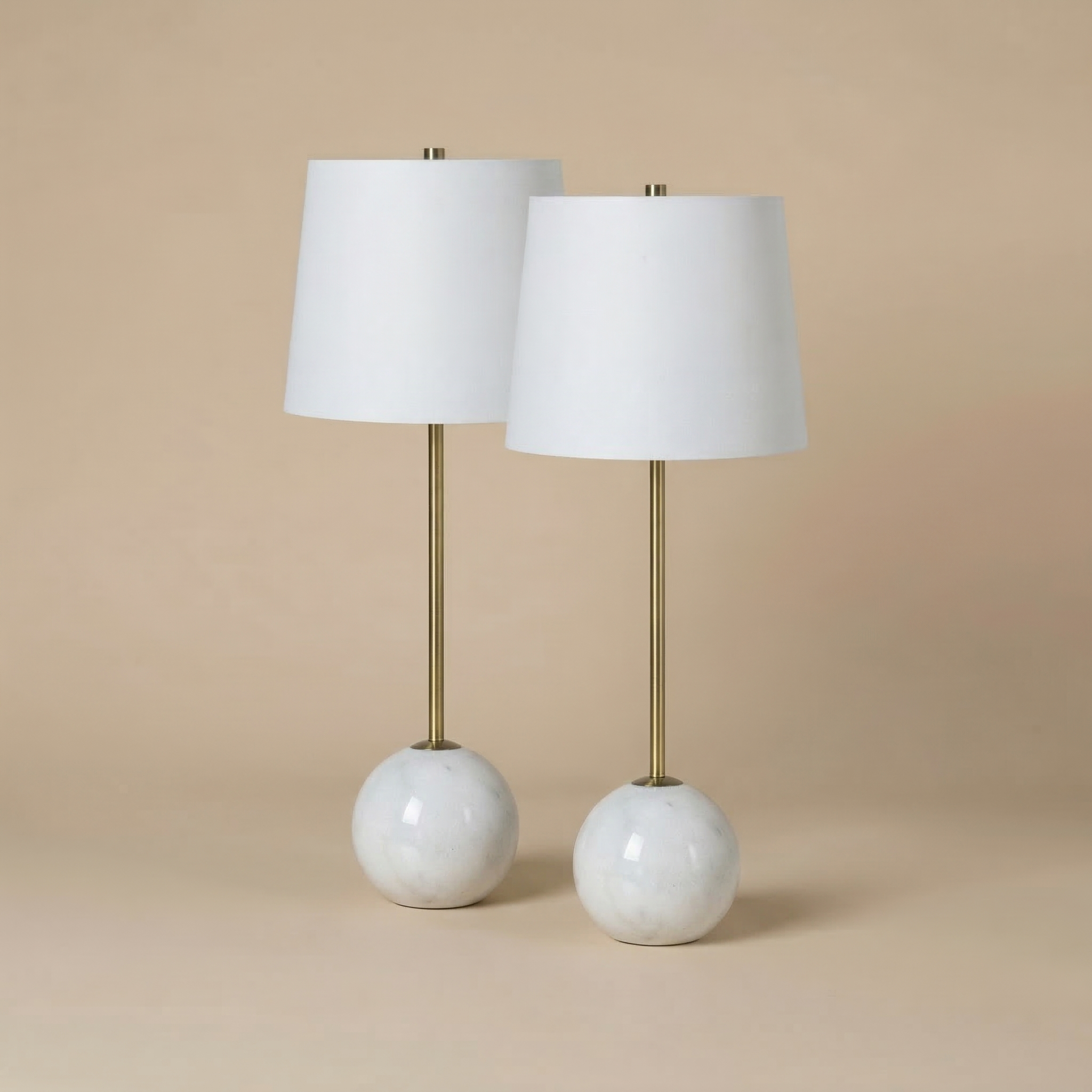 A set of two Nox table lamps featuring spherical white marble bases, slender brass stems, and white linen shades.