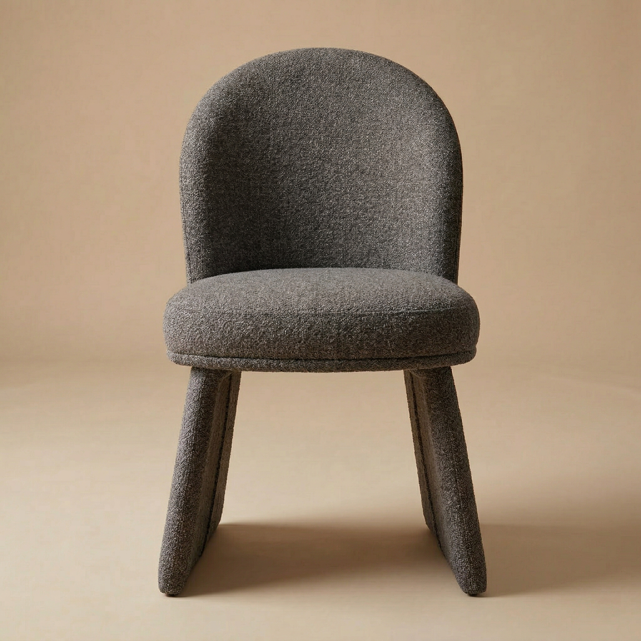 Full front view of the Odette bouclé chair in charcoal color fabric showcasing its curved backrest and unique monolithic upholstered base.