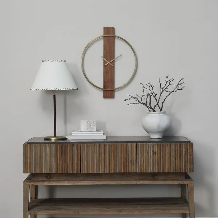 Orvella walnut and antique brushed brass wall clock displayed above a wood console with a table lamp and decorative vase.