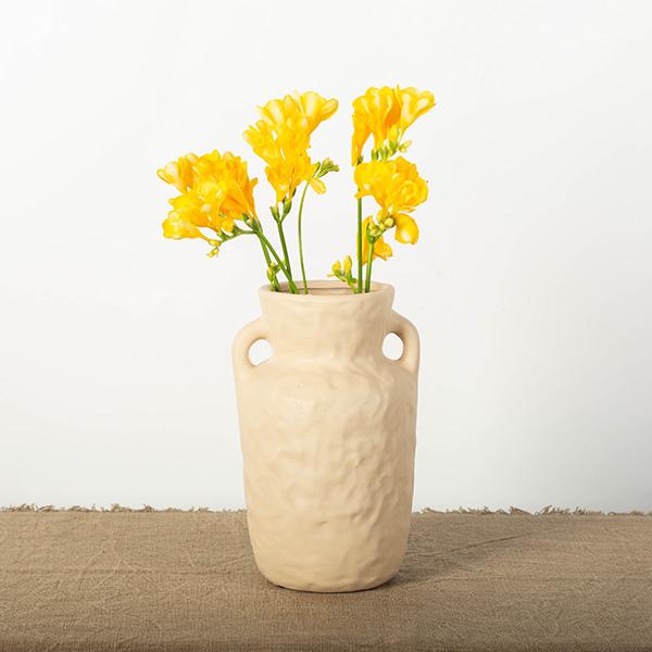 Beige textured vase with yellow flowers on a beige surface and white background