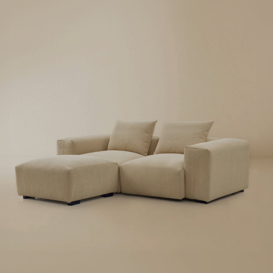 Beige plush corduroy modular sofa with two seater and ottoman configuration in a studio background