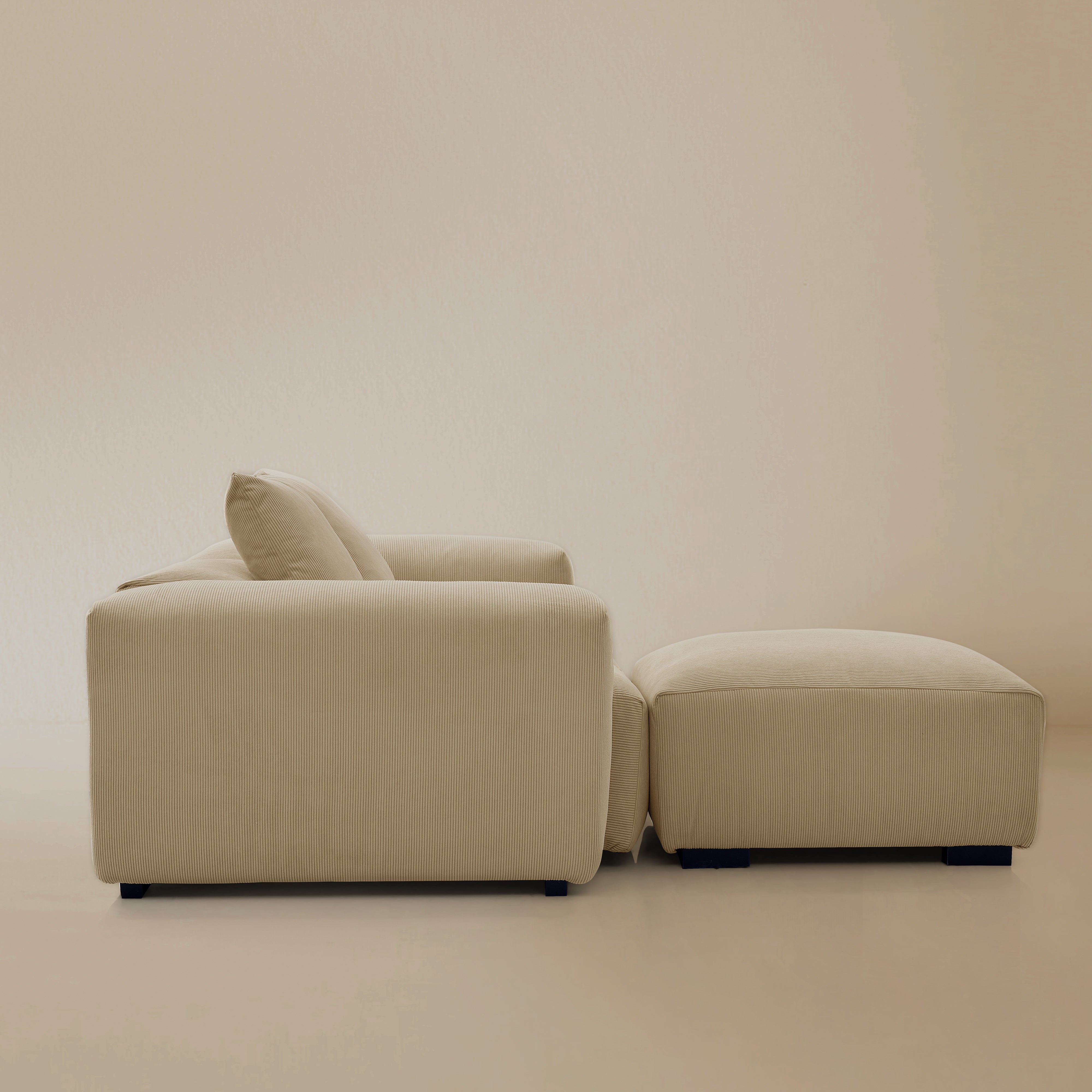 Side view of the two seater beige plush corduroy modular sofa with ottoman n a studio background