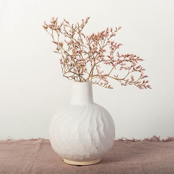 White textured vase with dried pink branches on a neutral background