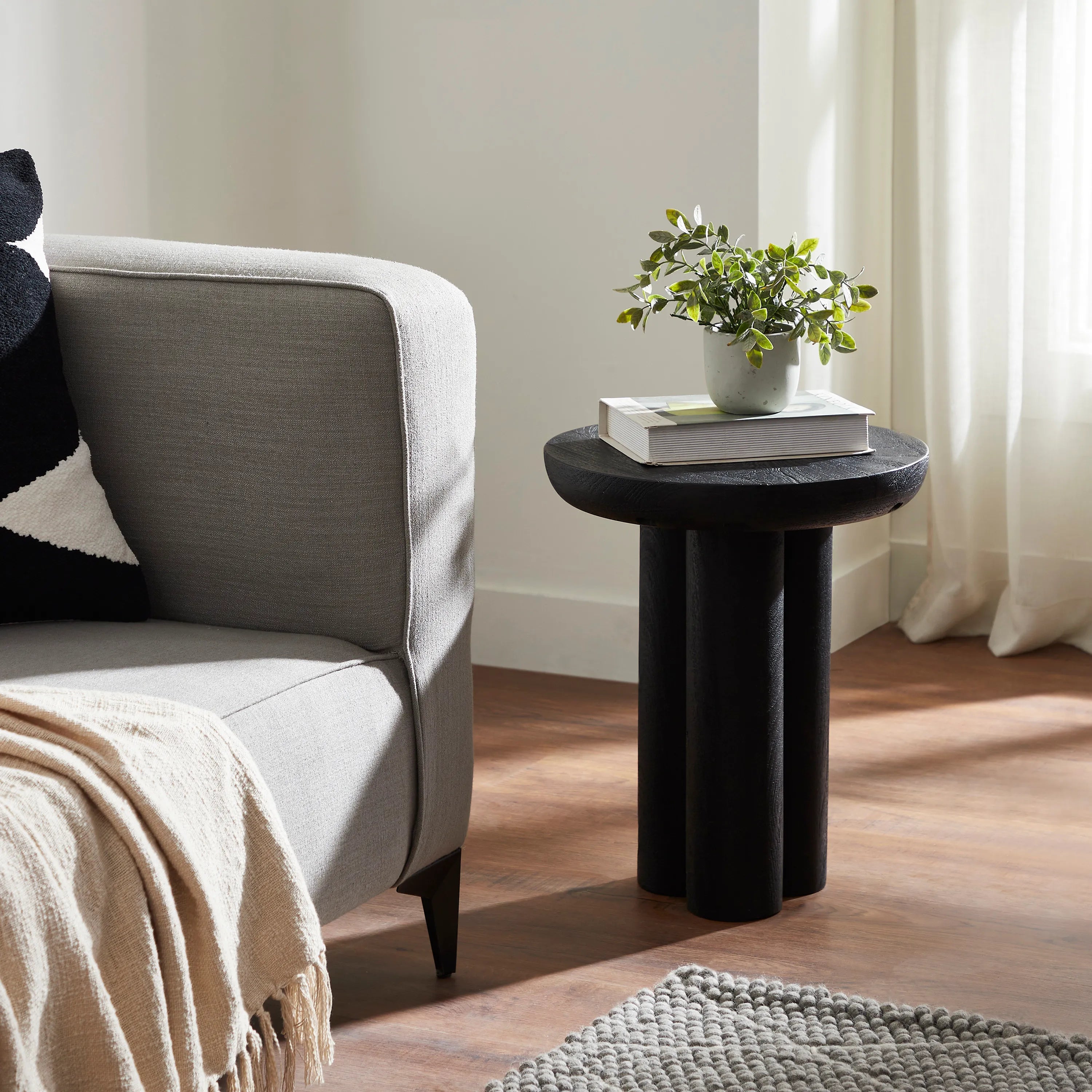 Black Ryn side table styled in a modern living room with a grey sofa, books, and greenery, showcasing its bold silhouette.