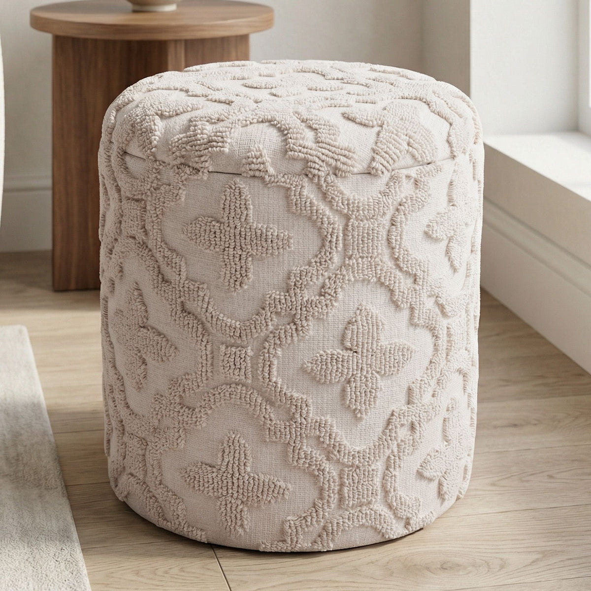 Textured beige ottoman on a wooden floor with a wooden table in the background