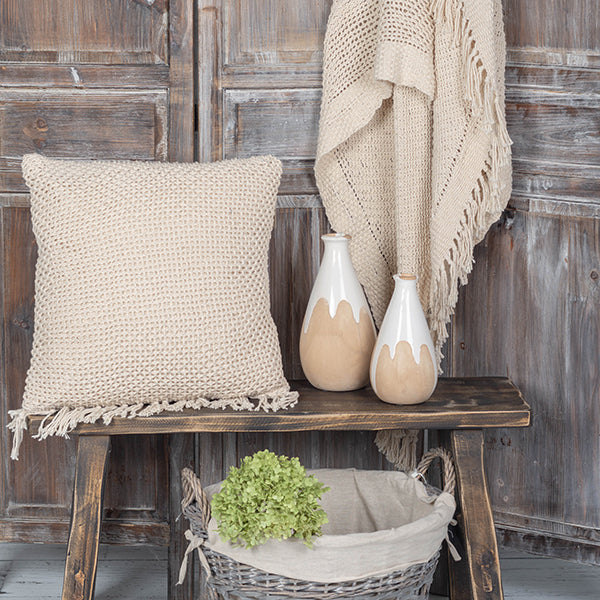 Decorative setting with a textured pillow, vases, and a basket on a wooden table against a rustic wooden wall.