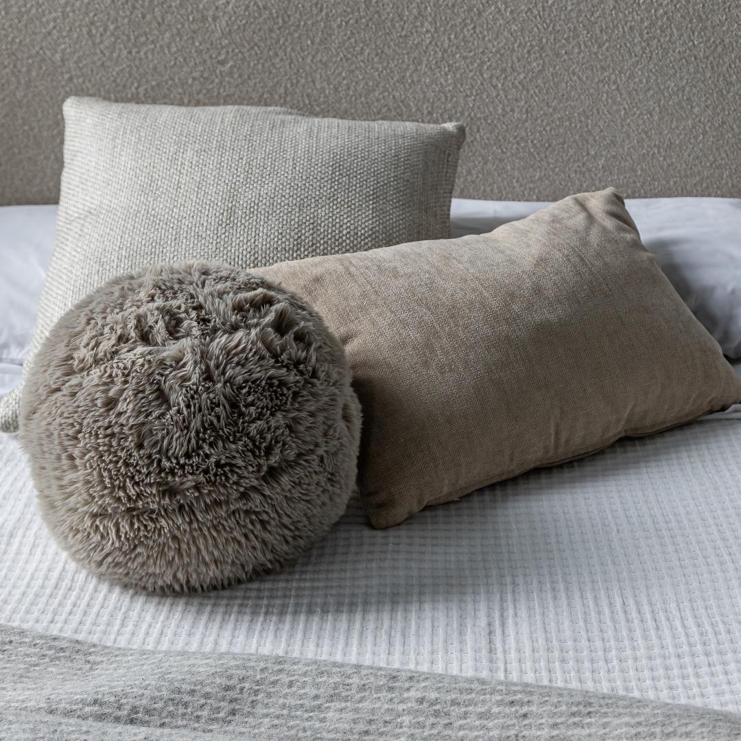 The Serenity natural cushion trio styled on a bed with a bouclé headboard and textured knit throw for a layered look.