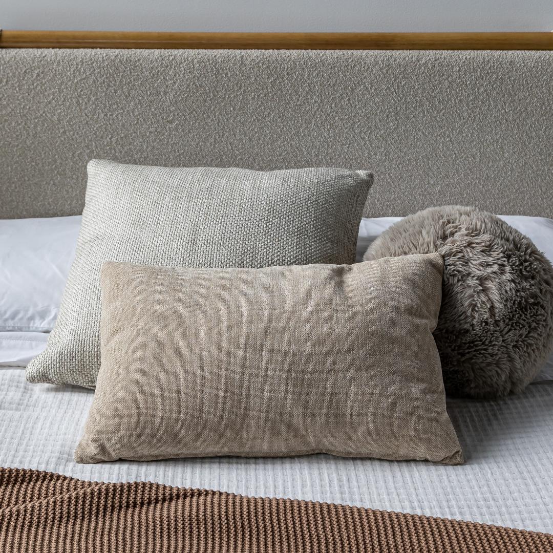 Close-up lifestyle view of the Serenity cushion set on white bedding, highlighting the blend of soft grey and tan natural tones.
