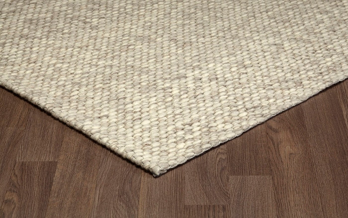 Corner view of the cream Silas hand-woven wool rug resting on a wooden floor, showcasing its textured edge